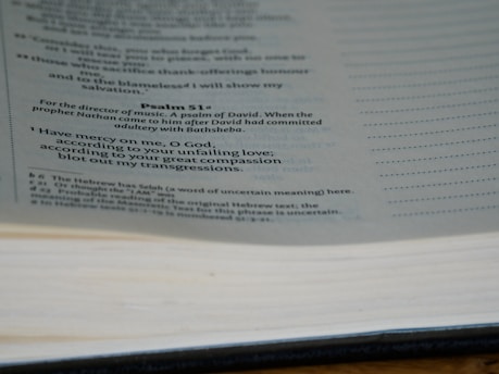 A close-up view of a Bible showing text from Psalm 51, specifically the beginning lines of the passage. The page includes annotations at the bottom with explanations and footnotes. The Bible text is printed in black on a light-colored page.