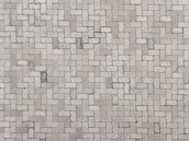 An arrangement of light gray interlocking paving stones forms a repetitive pattern. The pavers are rectangular with irregular, wavy edges, creating a uniform and structured surface.