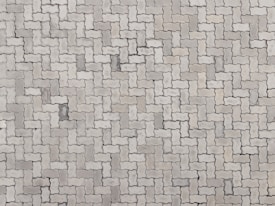 An arrangement of light gray interlocking paving stones forms a repetitive pattern. The pavers are rectangular with irregular, wavy edges, creating a uniform and structured surface.