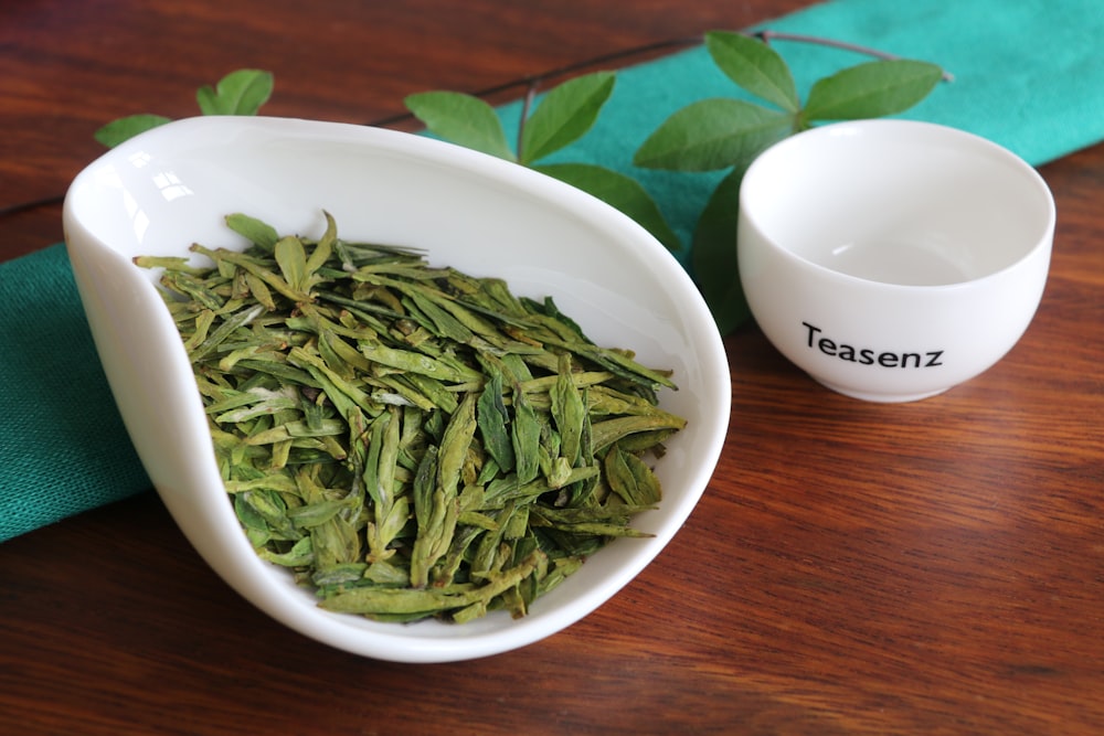 a bowl of green beans next to a white cup