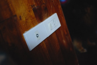 A wooden wall with a white electrical plate featuring two outlets, one with a coaxial socket and the other with a rotary dimmer switch.