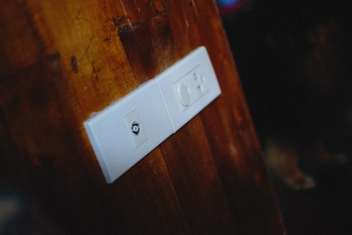 A wooden wall with a white electrical plate featuring two outlets, one with a coaxial socket and the other with a rotary dimmer switch.