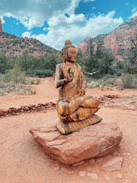 A close-up of a handcrafted medallion resting on red Sedona rocks with a scenic vortex site in the background.
