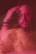 A blurred, artistic portrait of a person with a contemplative expression. The colors are predominantly pink and red, and the double exposure effect creates a sense of motion and ambiguity.