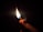 A hand is holding and lighting a matchstick. The flame is bright and contrasts starkly against the dark background, illuminating the hand and matchstick.