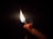 A hand is holding and lighting a matchstick. The flame is bright and contrasts starkly against the dark background, illuminating the hand and matchstick.