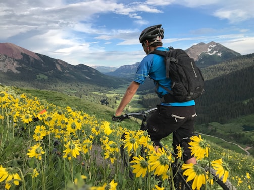 A cyclist pausing on a scenic mountain trail, looking at a map under a bright blue sky.