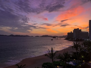 A panoramic sunset view over a tropical beach with palm trees and calm waves.