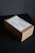 A cardboard box is placed on a dark surface. The box has a label on top with text related to personal delivery. Soft lighting creates subtle shadows around the box, emphasizing its shape and texture.