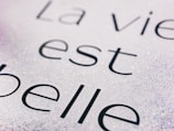 A close-up view of text on a sparkling background with the phrase 'La vie est belle' written in elegant black font. The surface appears to be glittery, creating a shimmering effect around the letters.
