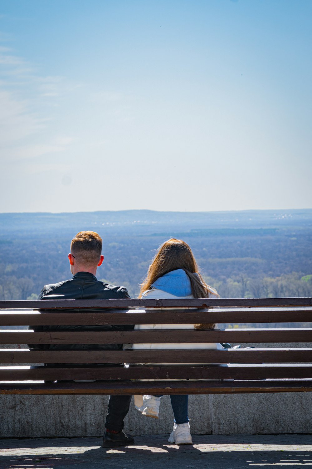a man and woman sitting on a bench overlooking a city