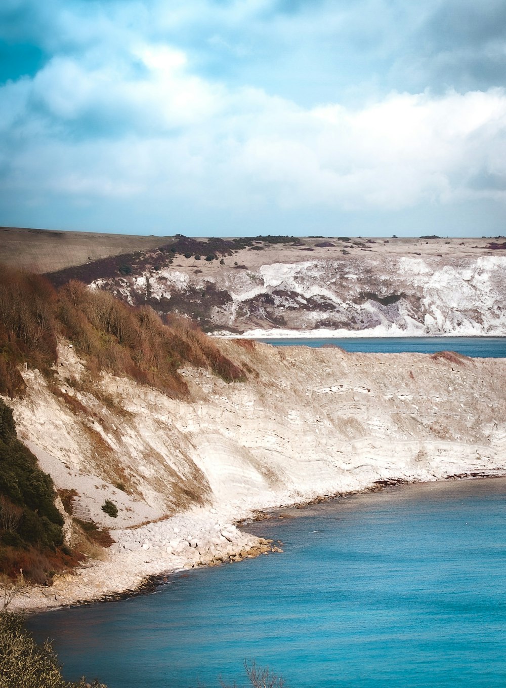 a body of water with a rocky shoreline and a blue sky