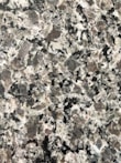 A close-up view of a granite surface with a coarse, speckled pattern. The stone features a mix of black, white, and gray crystals with some pinkish areas, giving it a textured and natural appearance.
