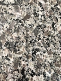 A close-up view of a granite surface with a coarse, speckled pattern. The stone features a mix of black, white, and gray crystals with some pinkish areas, giving it a textured and natural appearance.