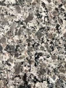 A close-up view of a granite surface with a coarse, speckled pattern. The stone features a mix of black, white, and gray crystals with some pinkish areas, giving it a textured and natural appearance.