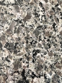 A close-up view of a granite surface with a coarse, speckled pattern. The stone features a mix of black, white, and gray crystals with some pinkish areas, giving it a textured and natural appearance.