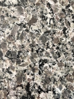 A close-up view of a granite surface with a coarse, speckled pattern. The stone features a mix of black, white, and gray crystals with some pinkish areas, giving it a textured and natural appearance.