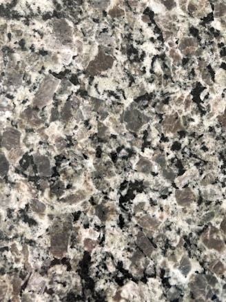 A close-up view of a granite surface with a coarse, speckled pattern. The stone features a mix of black, white, and gray crystals with some pinkish areas, giving it a textured and natural appearance.