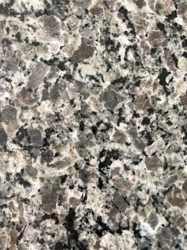 A close-up view of a granite surface with a coarse, speckled pattern. The stone features a mix of black, white, and gray crystals with some pinkish areas, giving it a textured and natural appearance.