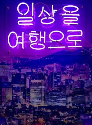 A modern cityscape at night, illuminated with neon lights from a Kdrama.