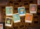 A collection of trading cards from a game called 'Toons and Towers' is spread out on a wooden surface. Each card features a colorful cartoon character and various stats like class, attack, and defense. The characters include a bird, a mushroom, a pig, a chameleon, a cat, and a large bird-like creature.