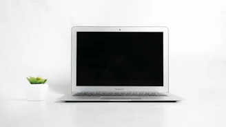 A sleek white Purelia air purifier gently glowing on a modern office desk beside a laptop and a potted plant.