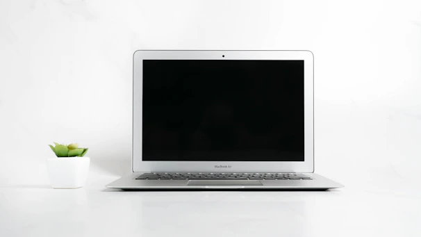 A sleek white Purelia air purifier gently glowing on a modern office desk beside a laptop and a potted plant.