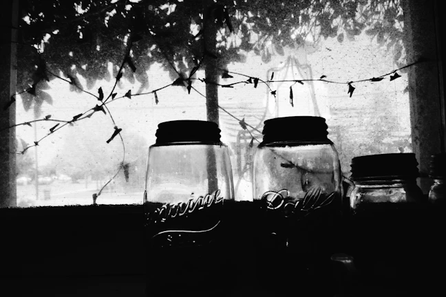 Sunlight filtering through a window onto jars of homemade vinegar aging in clay pots.
