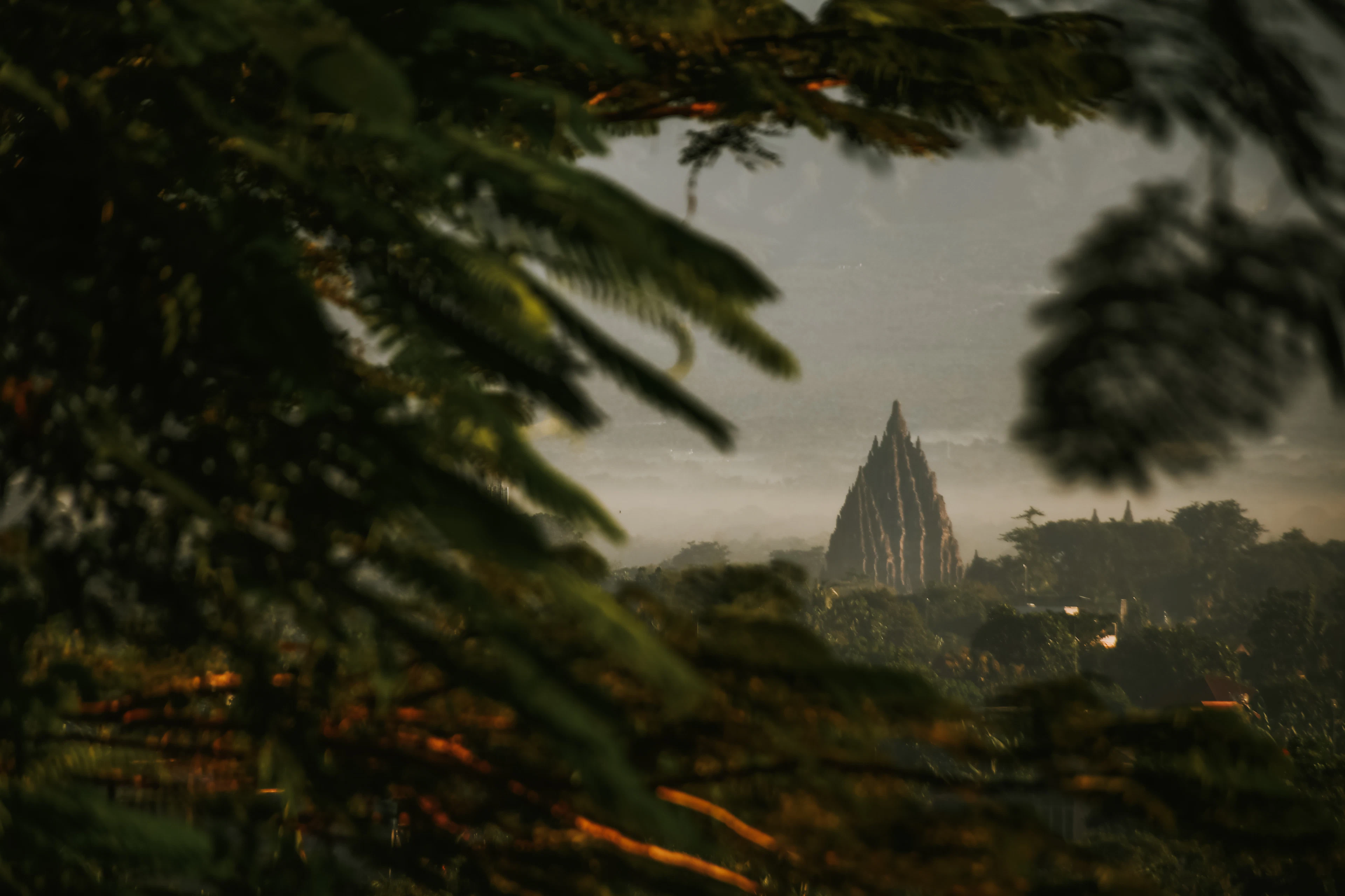 The spire of Prambanan temple in the evening dusk, seen through the foliage, Yogyakarta
