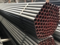 A stack of metal pipes, neatly arranged and secured with straps. The pipes have a uniform cylindrical shape and are aligned horizontally across the image. The visible ends of the pipes show a reddish tint, contrasting with the darker metal body.