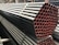 A stack of metal pipes, neatly arranged and secured with straps. The pipes have a uniform cylindrical shape and are aligned horizontally across the image. The visible ends of the pipes show a reddish tint, contrasting with the darker metal body.