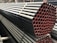 A stack of metal pipes, neatly arranged and secured with straps. The pipes have a uniform cylindrical shape and are aligned horizontally across the image. The visible ends of the pipes show a reddish tint, contrasting with the darker metal body.