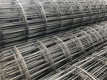 Rolls of wire mesh and spools of wire stacked in a warehouse.