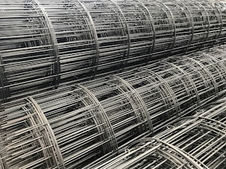 Multiple rolls of metallic wire mesh are tightly wound and stacked together, showcasing an industrial and geometric pattern.