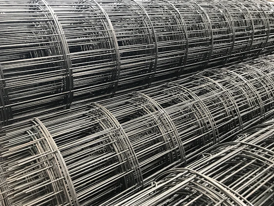 Close-up of shimmering stainless steel wire mesh rolls stacked in a bright Canadian warehouse.