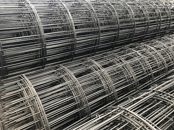 Multiple rolls of metallic wire mesh are tightly wound and stacked together, showcasing an industrial and geometric pattern.