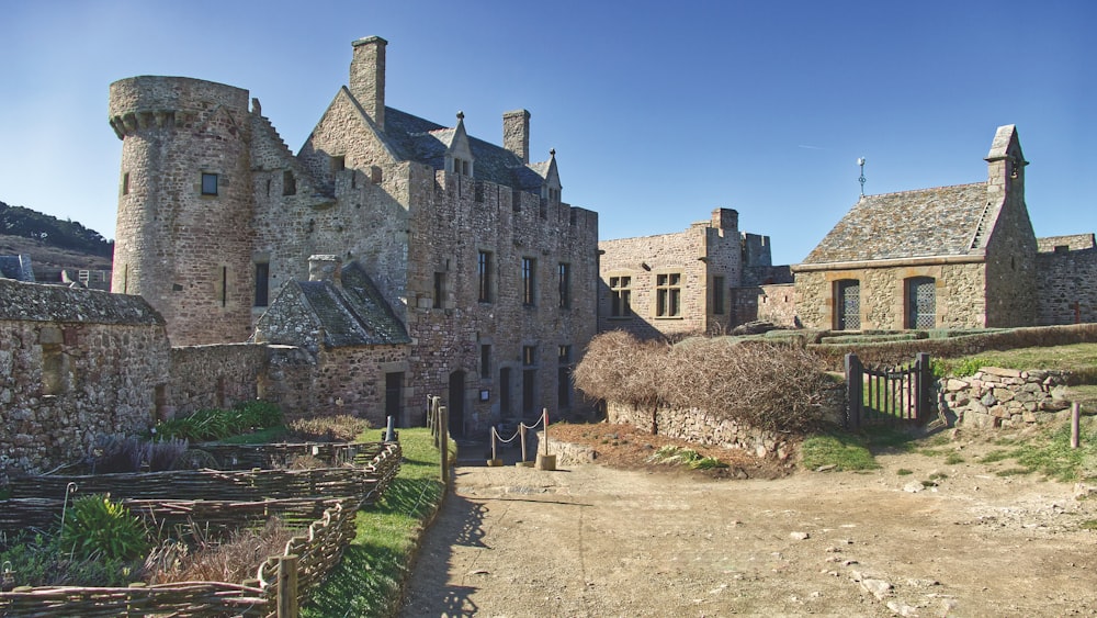 a stone building with a fence and bushes in front of it