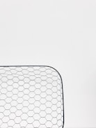 A close-up view of a hexagonal wire mesh, likely made of metal, against a white background. The mesh forms a curved rectangular shape, consisting of evenly spaced hexagonal patterns.