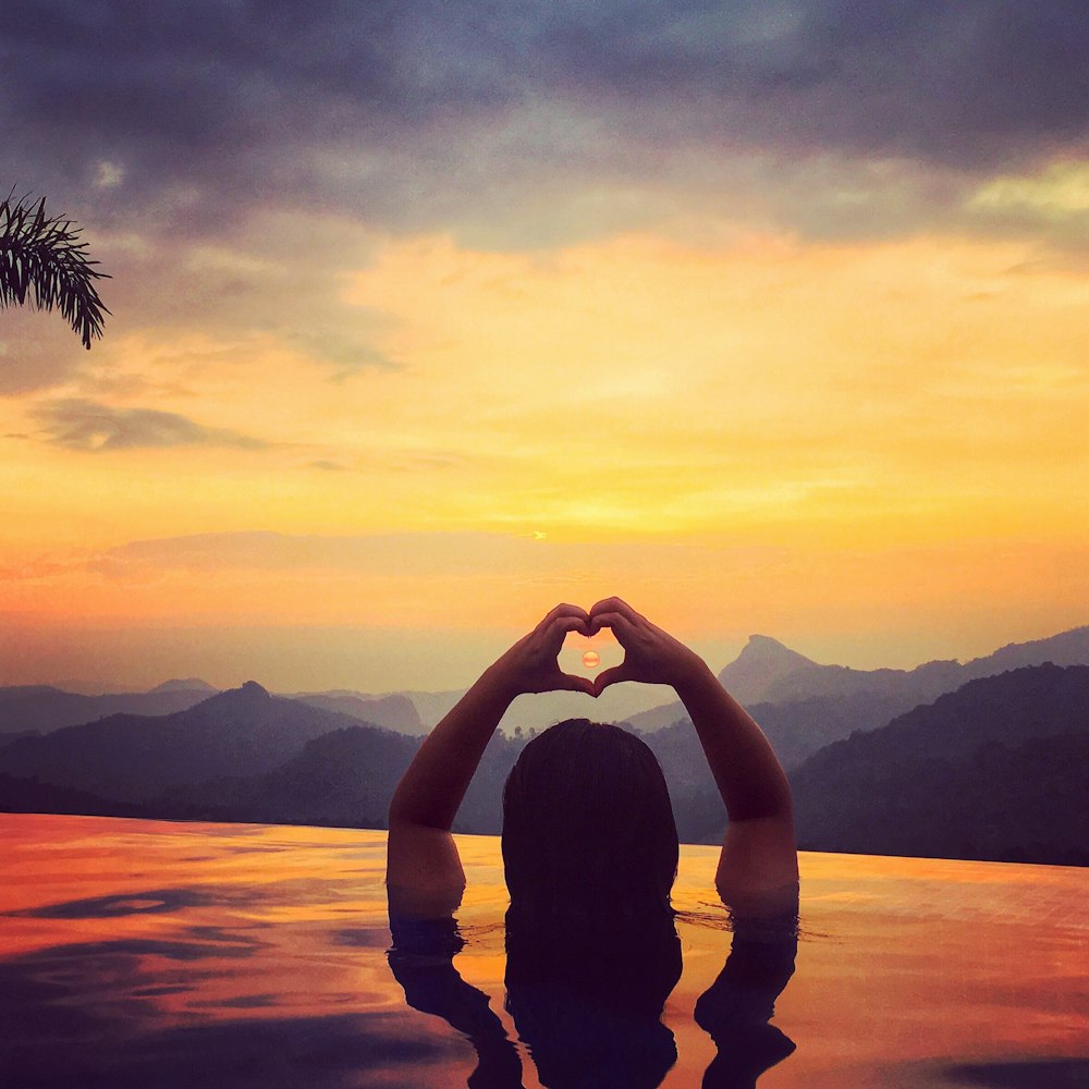 a person holding the hands up in front of a sunset