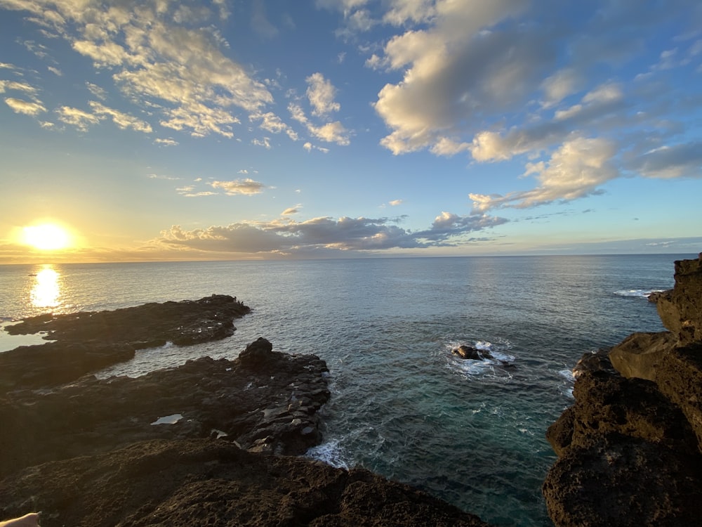 a body of water with rocks and a sunset