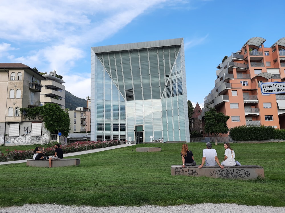 a group of people sitting on a bench in front of a glass building