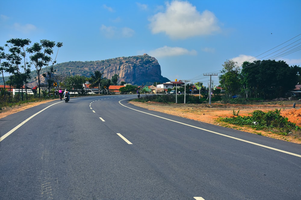 a person riding a motorcycle on a road with trees and mountains in the background