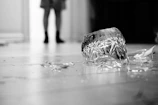 Close-up of shattered dishes on the floor with a blurred figure in the background holding a bat ready to break more.