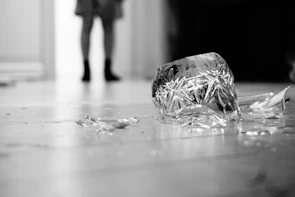Close-up of shattered dishes on the floor with a blurred figure in the background holding a bat ready to break more.