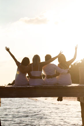 a group of people sitting on a dock with their hands up