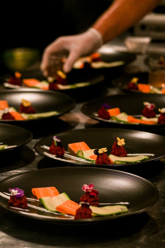 Hands preparing food on a bare wooden table, ingredients arranged with intention.