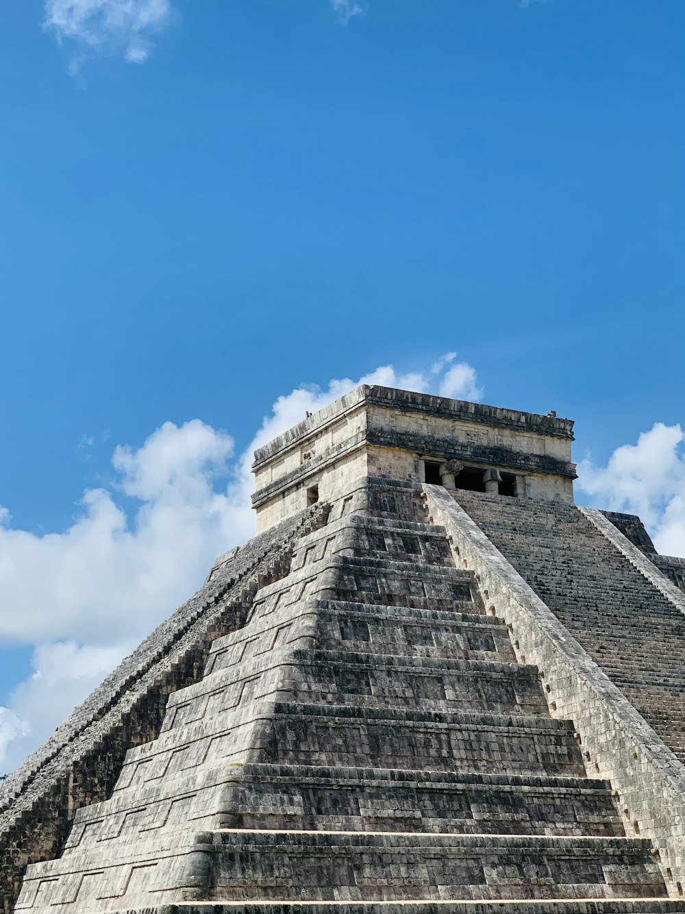 a stone pyramid with a blue sky with Chichen Itza in the background