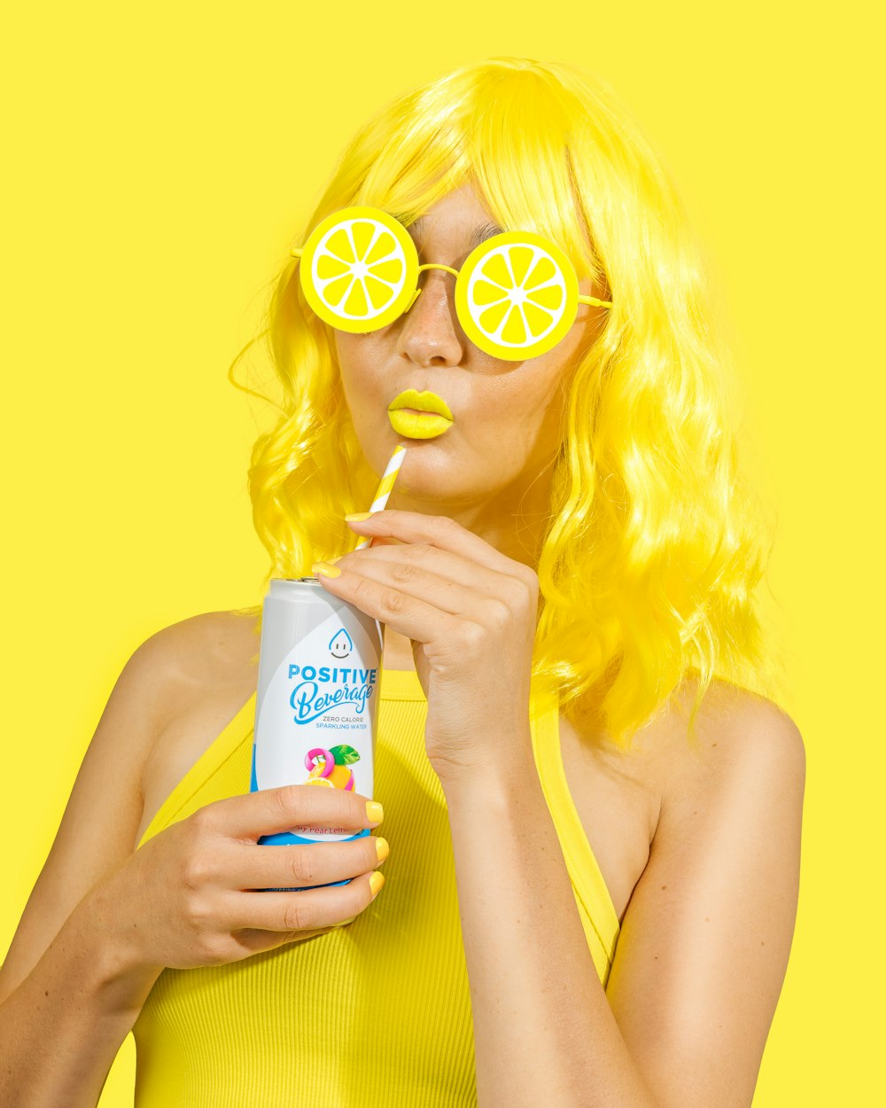 a woman wearing yellow glasses and a yellow wig drinking from a can
