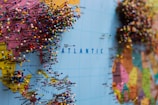 A map of the world with numerous colorful push pins concentrated around the eastern United States and Europe. The pins are densely packed, suggesting popular or significant locations. The map displays clear geographic markings and labels on the Atlantic Ocean, with visible continents.