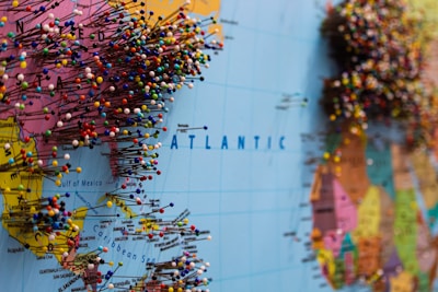 A map of the world with numerous colorful push pins concentrated around the eastern United States and Europe. The pins are densely packed, suggesting popular or significant locations. The map displays clear geographic markings and labels on the Atlantic Ocean, with visible continents.